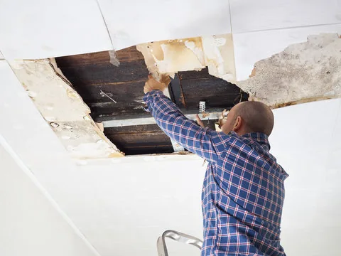 Man pulling down a sagging, water-damaged ceiling panel after a leak